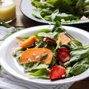 Greens, Persimmon Ricotta Salad with Orange Dressing garnished with ricotta and served in a white plate.
