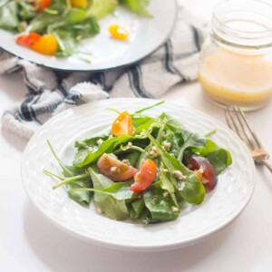 Spinach, Heirloom Tomato and Crumbled Tofu Salad with Roasted Garlic Dressing served in a white bowl.