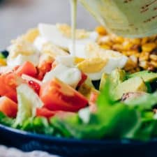 creamy avocado blue cheese dressing being poured on cobb salad