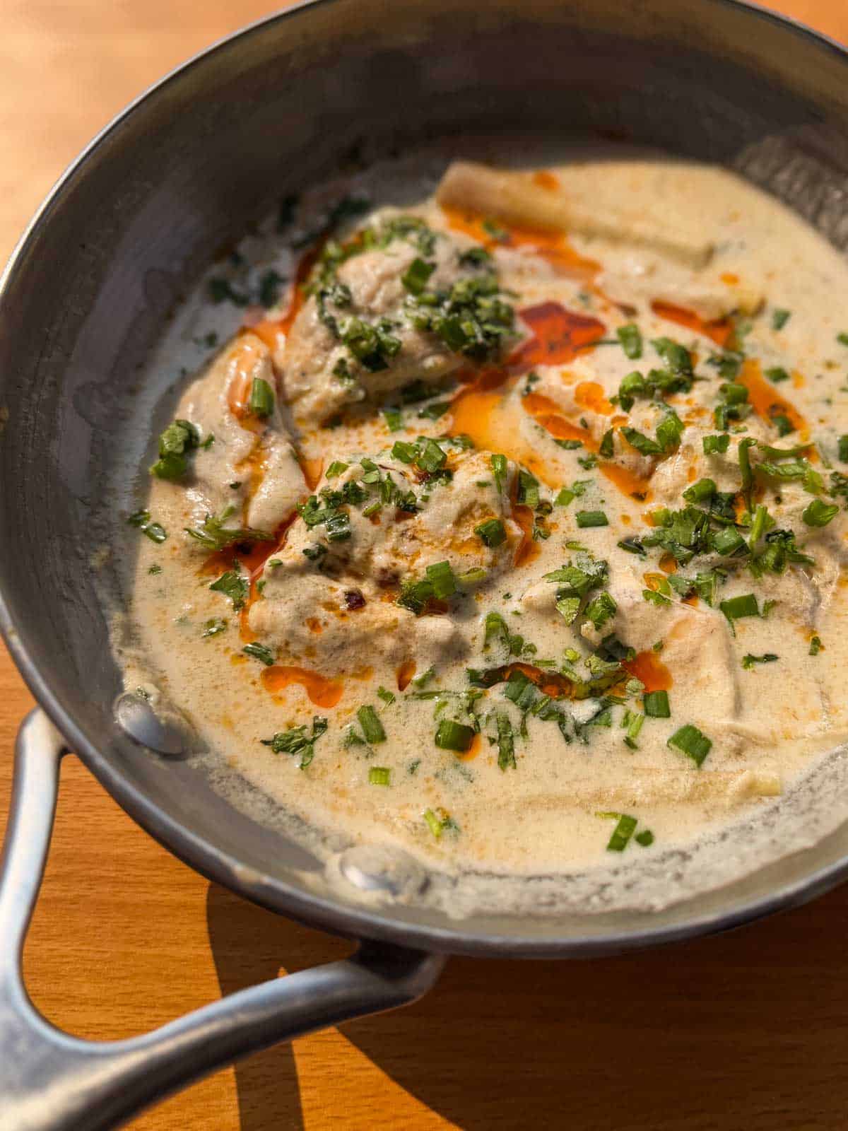 thai poached fish in coconut milk topped with chilli oil and spring onions served in a pan