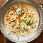 thai poached fish in coconut milk topped with chilli oil and spring onions served in a pan
