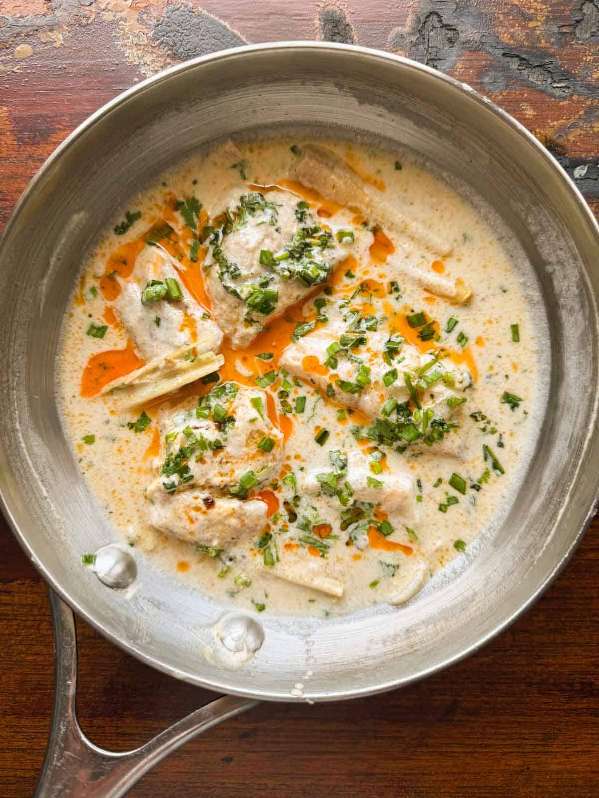 thai poached fish in coconut milk topped with chilli oil and spring onions served in a pan