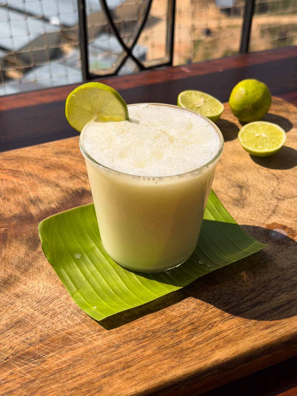 A picture of limonada served in a glass with a lime slice on the side. The glass is kept on a banana leaf