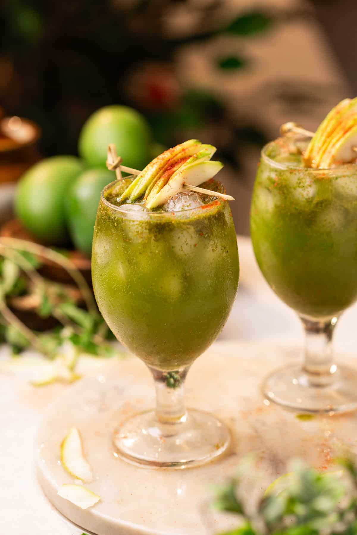 two glasses of aam panna garnished with raw mango slices and chilli powder