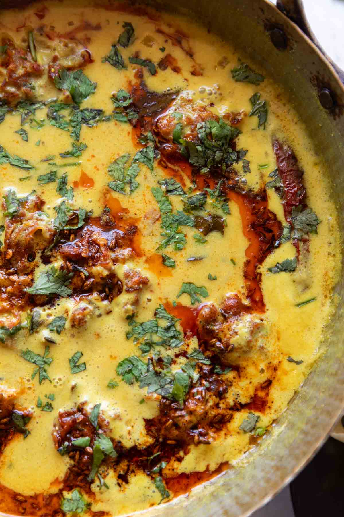 vibrant kadhi pakora garnished with a tadka and coriander leaves, served in a copper handi