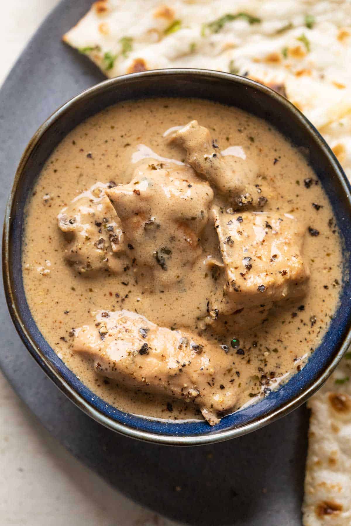 Chicken kali mirch gravy served in a blue bowl with naan on the side