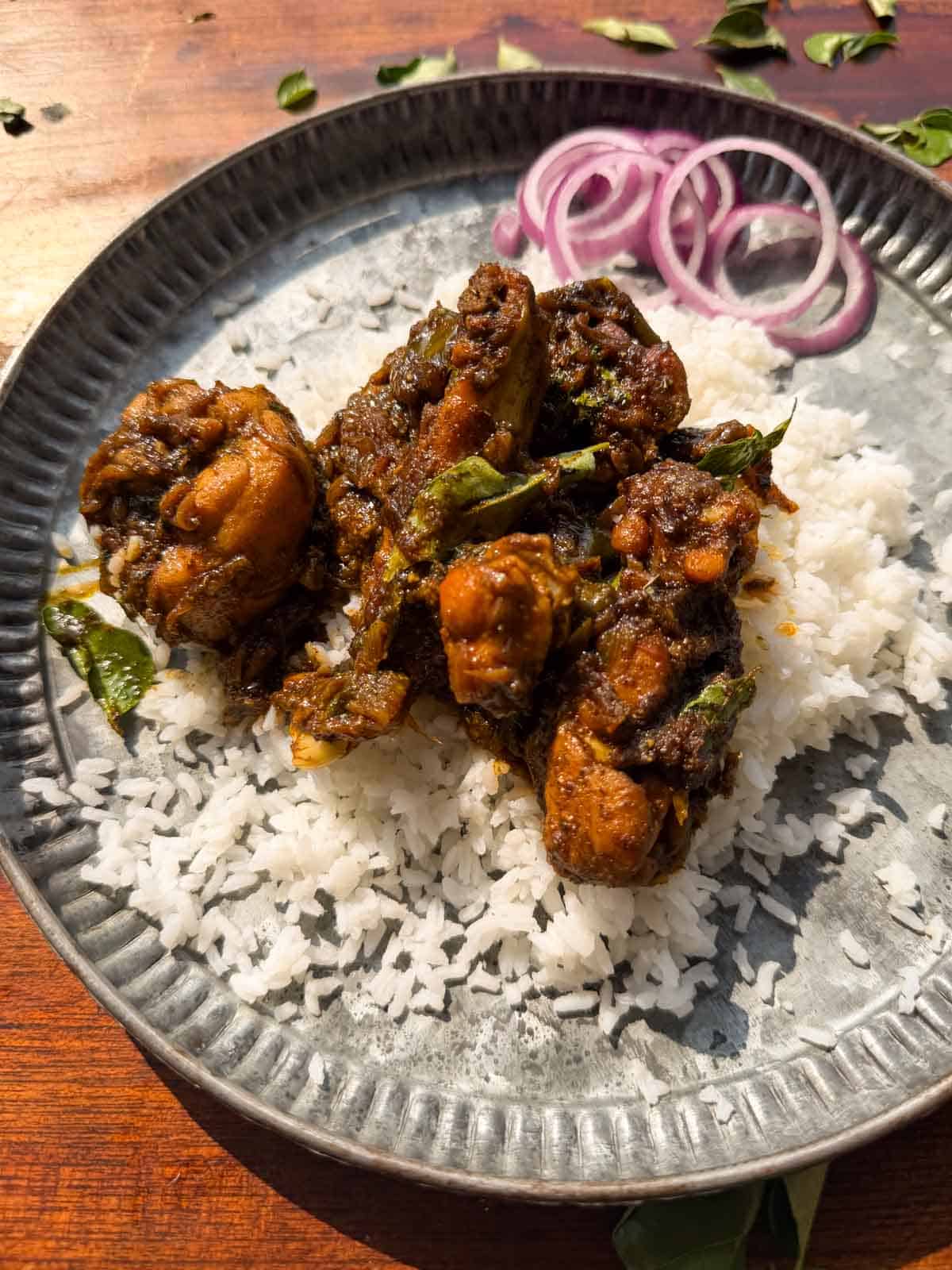 an image of curry leaf chicken served on a bed of rice with sliced onions on the side