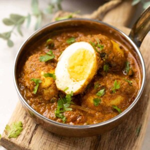 shot of egg curry in a steel bowl topped with coriander leaves