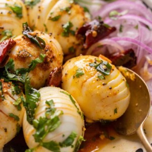 Close up of hasselback egg tadka with a spoon and sliced onions on the side