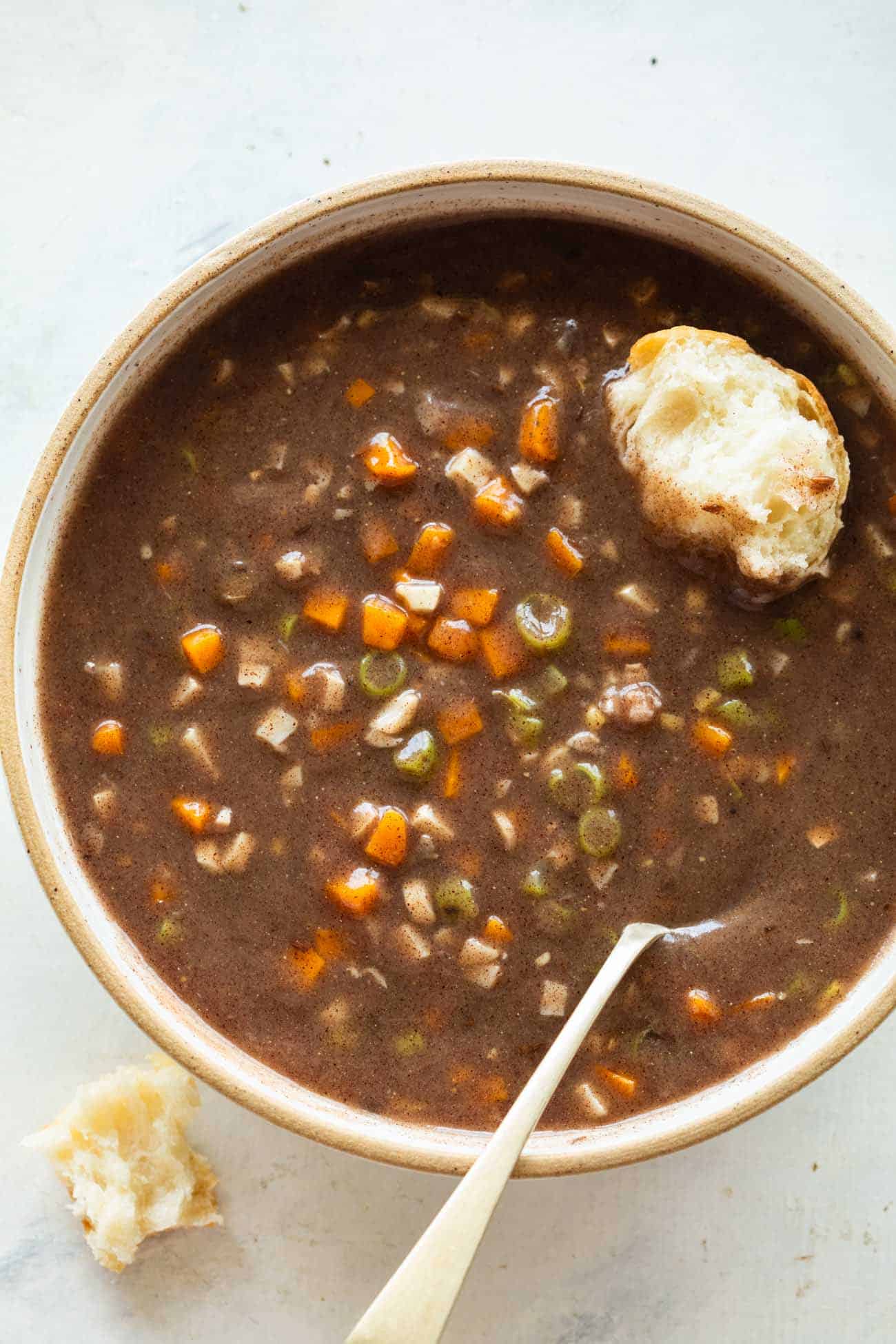 a whole bowl with ragi soup with diced carrots and beans with a spoon and a piece of bread dipped in the soup
