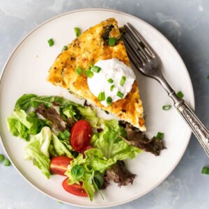A slice of spinach potato veggie frittata topped with a dollop of sour cream and chopped green onions