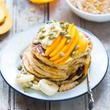 The pancakes topped with seeds, hung curd, sliced mangoes and served on a white plate.