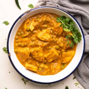 shot of matar paneer gravy in a white bowl with coriander sprinkled on top