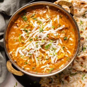 Picture of paneer lababdar served in a copper kadhai with naan on the side