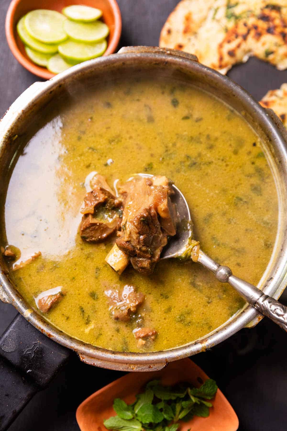 mutton marag in a bowl with a piece of chicken scooped up in a spoon to show texture