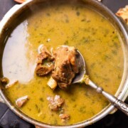 mutton marag in a bowl with a piece of chicken scooped up in a spoon to show texture