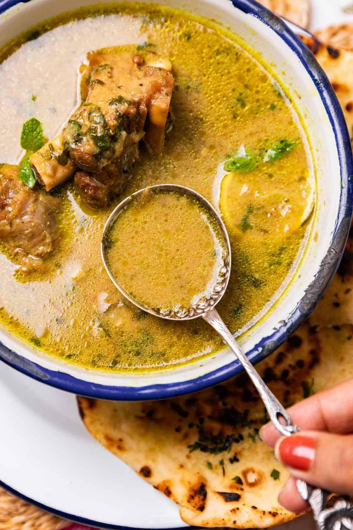 a spoon of mutton marag over a bowl of soup served with accompaniments to show the texture