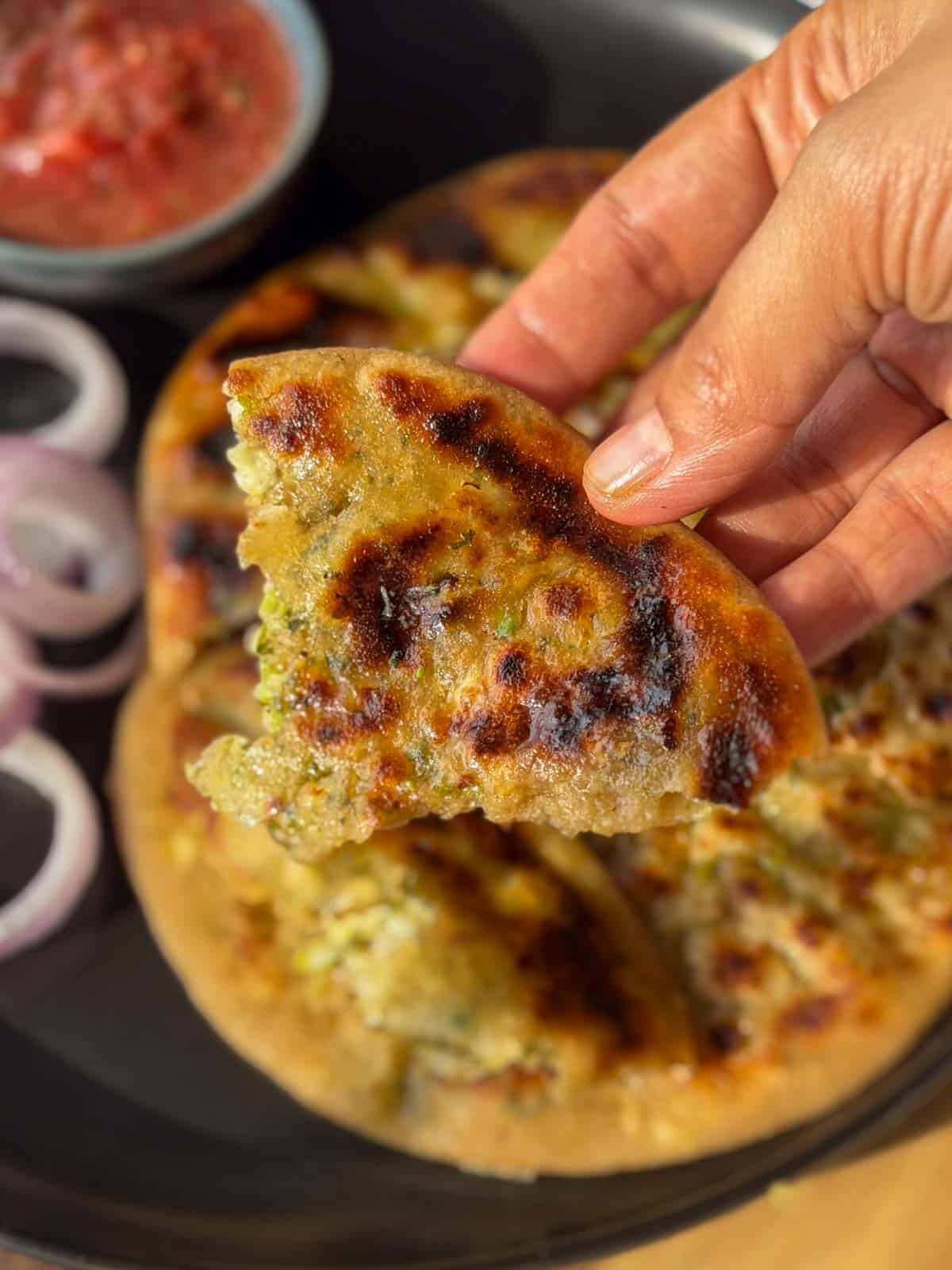 a person holding a piece of cook broccoli paneer paratha to showcase it's color and texture
