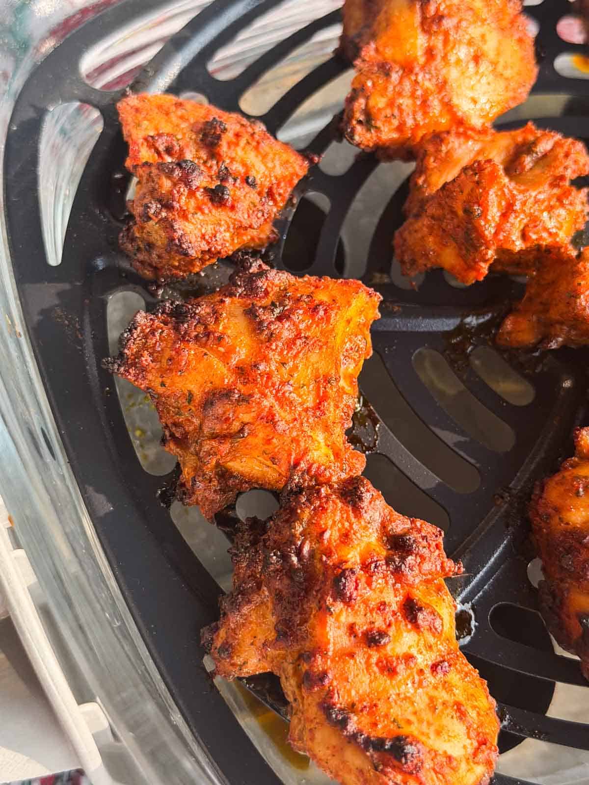 a close up image of tandoori chicken bites in the air basket